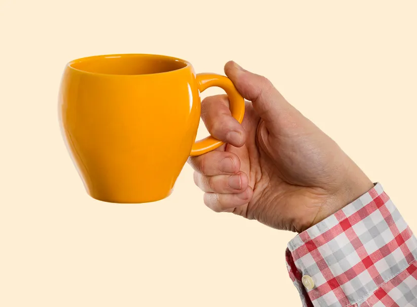 Mano sosteniendo una taza amarilla como símbolo de calidez navideña, perfecta para ilustrar momentos especiales con descuentos navideños.